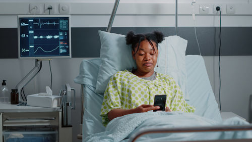 Portrait of young woman using mobile phone while sitting on bed at home