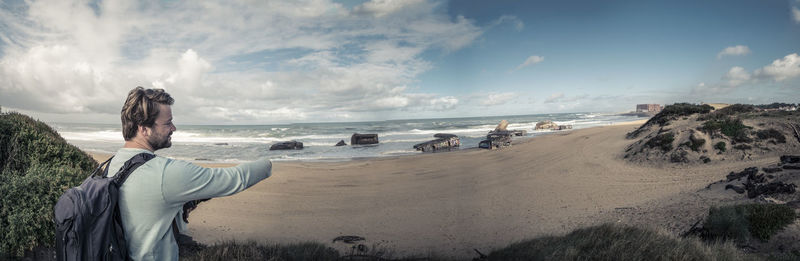 Panoramic view of young man standing at beach against sky