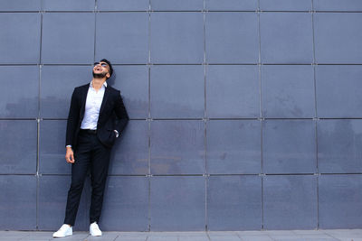 Young man looking away while standing against wall