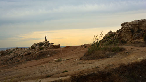 Mid distance of man standing on rock against sea during sunset