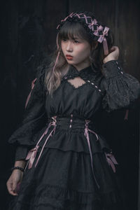 Portrait of young woman standing against black background