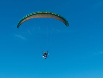 Low angle view of person paragliding against blue sky