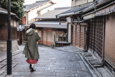 Rear view of woman wearing raincoat walking on street amidst buildings