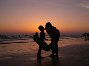 Silhouette friends on beach against sky during sunset