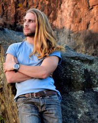 Man with long hair standing against rock