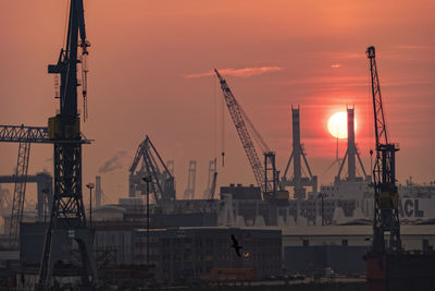 Cranes at commercial dock against sky during sunset