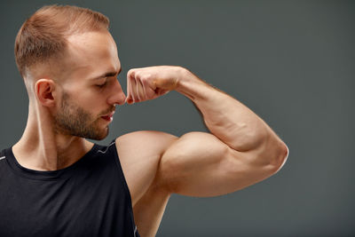 Young man flexing muscles against black background