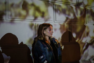 Smiling young woman standing by wall at night