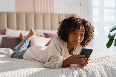 Young woman using mobile phone while sitting on bed at home