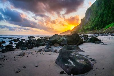 Rocks on beach against sky during sunset