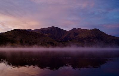 Scenic view of lake by mountains against sky during sunset