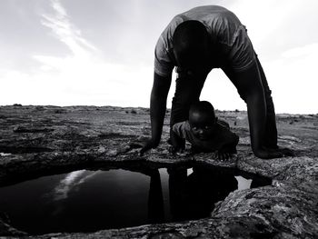 Rear view of silhouette man on rock against sky