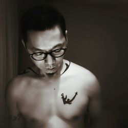 Close-up of shirtless tattooed young man standing against wall