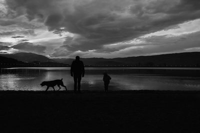 Silhouette people with dog standing on lake against sky