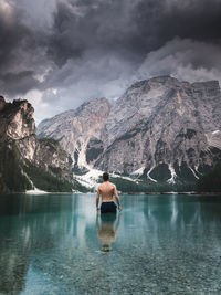 Rear view of shirtless man standing against mountain in lake