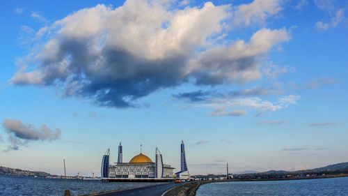 View of city at waterfront against cloudy sky