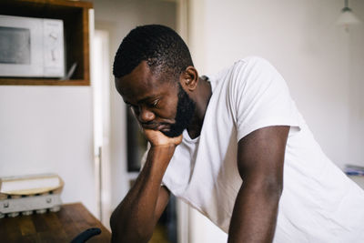 Thoughtful lonely man with hand on chin leaning in kitchen at home