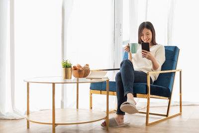 Young woman using phone while sitting on chair