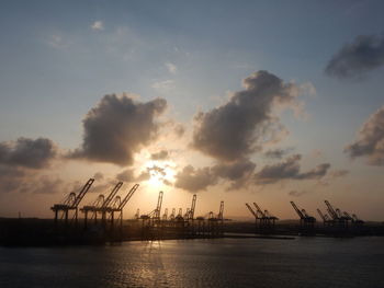 Silhouette of cranes at dock against cloudy sky