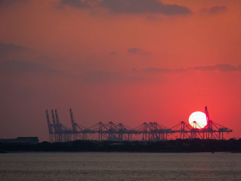 Silhouette cranes against orange sky during sunset