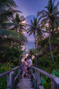 Rear view of women on walkway by palm trees against sky