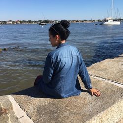 Rear view of woman sitting on retaining wall against sea