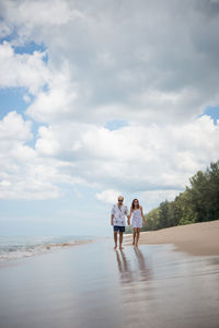 Man and woman walking at beach against sky