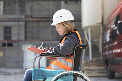 Woman wearing reflective vest and hard hat sitting in wheelchair taking notes