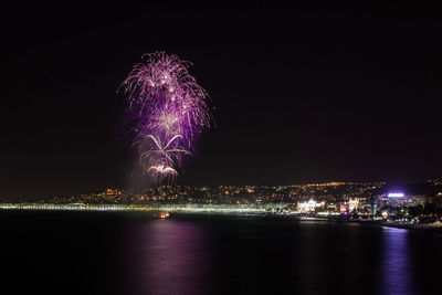 Firework display over illuminated city against sky at night