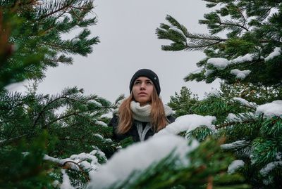 Woman looking away standing amidst trees during winter