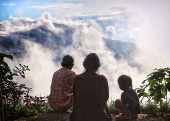Rear view of family sitting on mountain during foggy weather