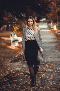 Portrait of smiling young woman standing at public park during autumn