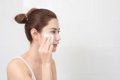 Side view of young woman cleaning face while standing in bathroom