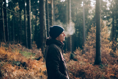 Side view of young man standing in forest