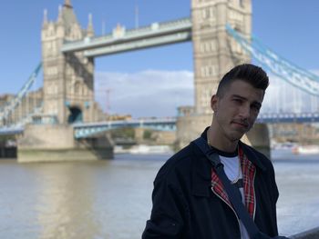 Portrait of young man standing against tower bridge