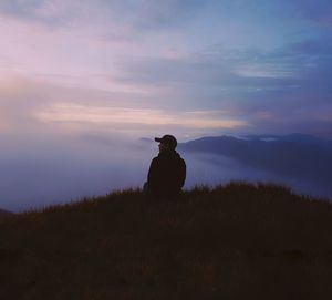 Rear view of silhouette man sitting on land against sky during sunset