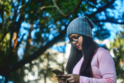 Low angle view of young woman using mobile phone while standing at park