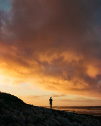 Silhouette man standing on street against sky during sunset