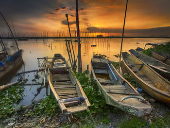 Abandoned boats moored at harbor against sky during sunset