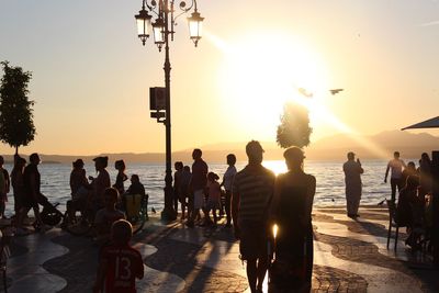 People standing on beach against sky during sunset