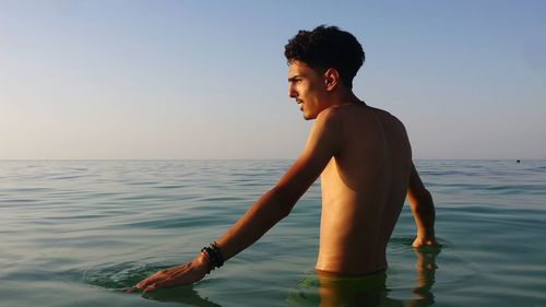 Shirtless young man standing in sea against sky