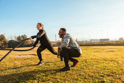 Woman exercising with rope by instructor on land against sky in sunny day