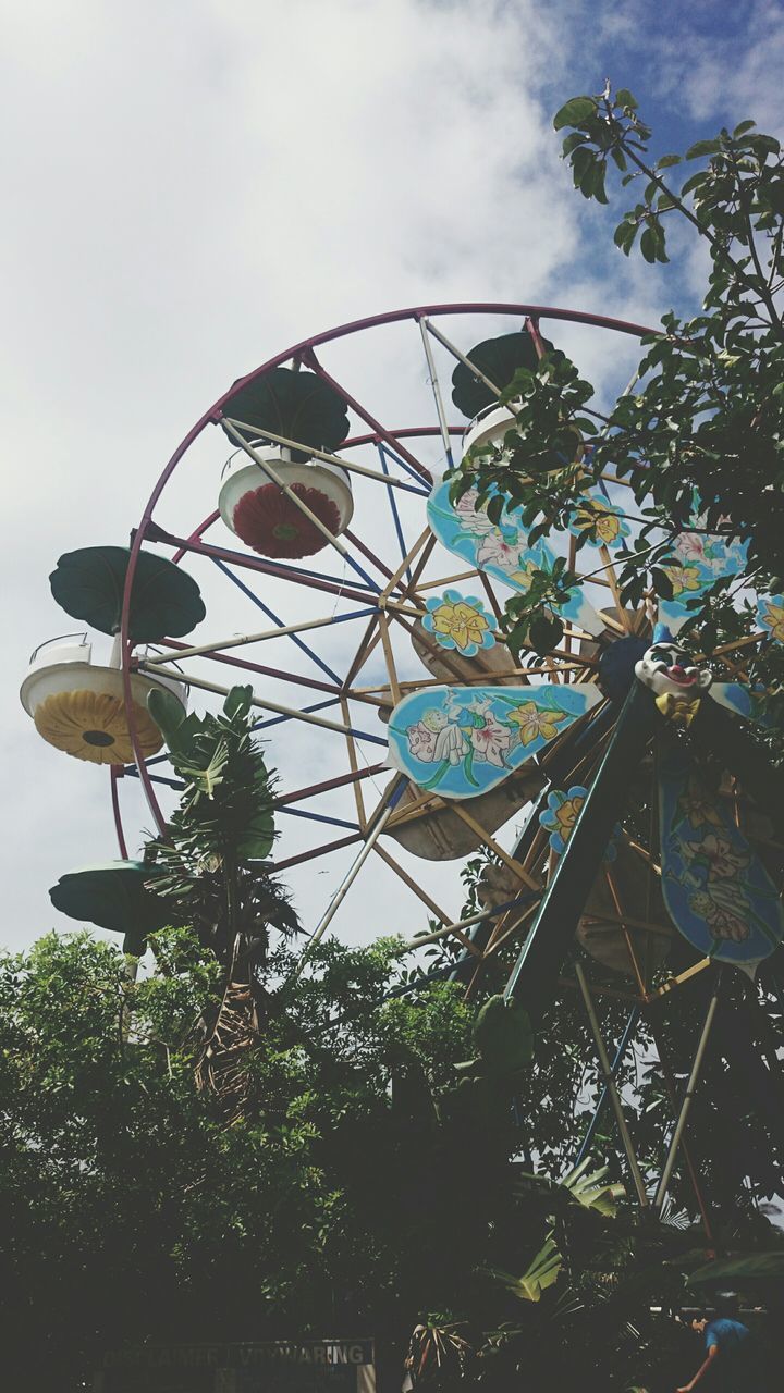 low angle view, sky, amusement park, ferris wheel, built structure, tree, amusement park ride, architecture, building exterior, arts culture and entertainment, day, hanging, outdoors, lighting equipment, no people, decoration, clear sky, city, growth, cloud - sky