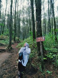 Full length of woman sitting by tree trunk with text in forest