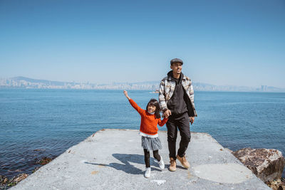 Full length of young woman standing against sea