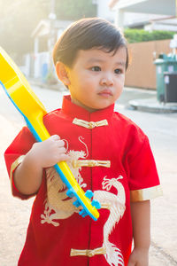 Cute boy holding toy guitar while standing on road