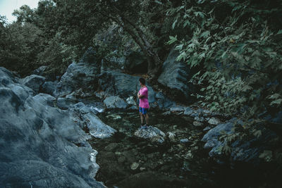 Rear view of woman walking on rock in forest