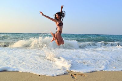 Excited woman jumping on shore at beach against sky