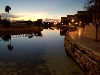 River by illuminated city against sky at sunset