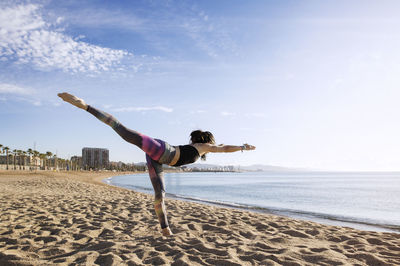 Determined woman performing yoga in warrior 3 pose on beach